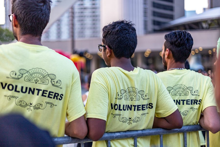 Voluntários de camiseta amarela acompanhando um evento na rua, vistos de costas
